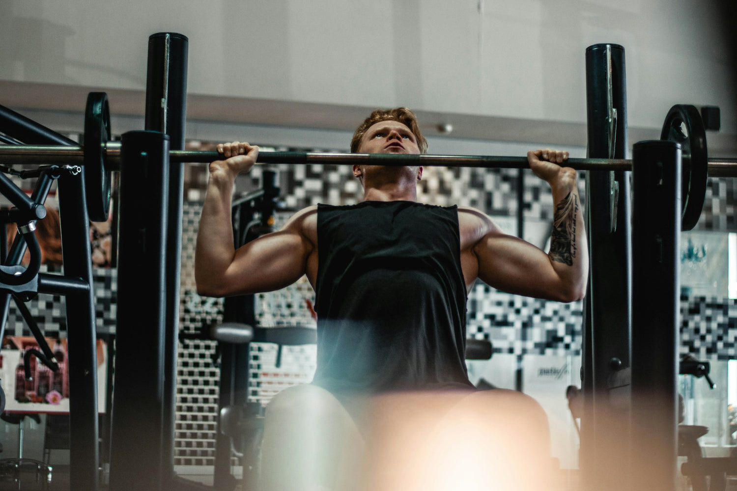 A man in a black tanktop lifting weights at the gym.