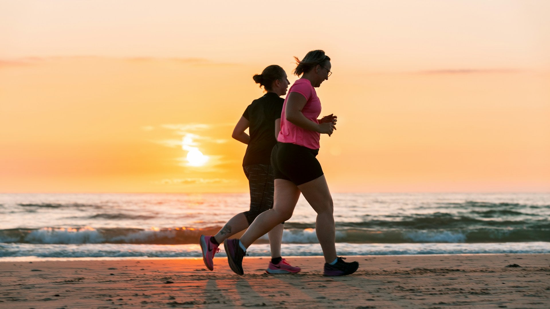 Two women jogging on the beach at sunrise.