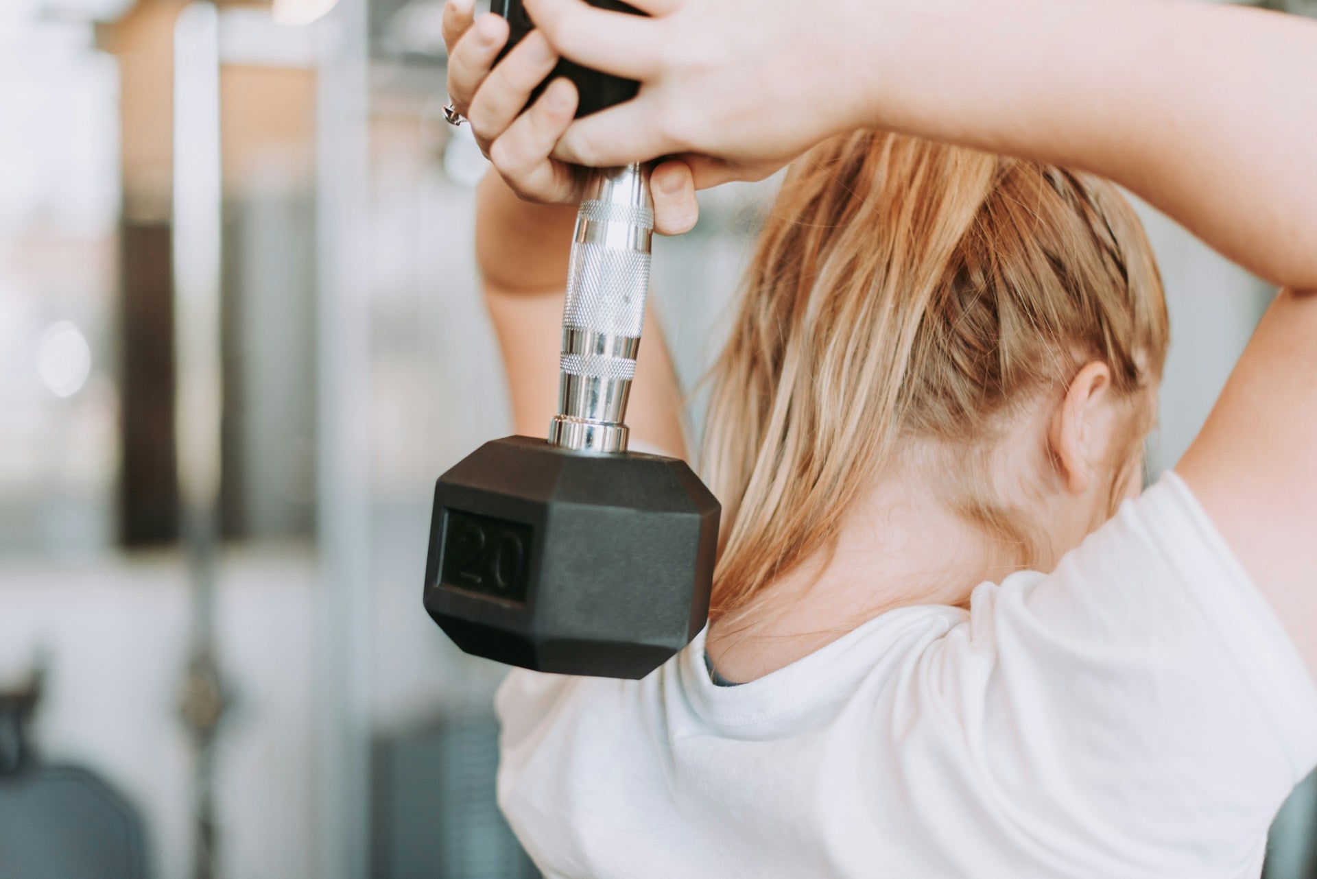 A woman in a white shirt lifting a weight in a gym.