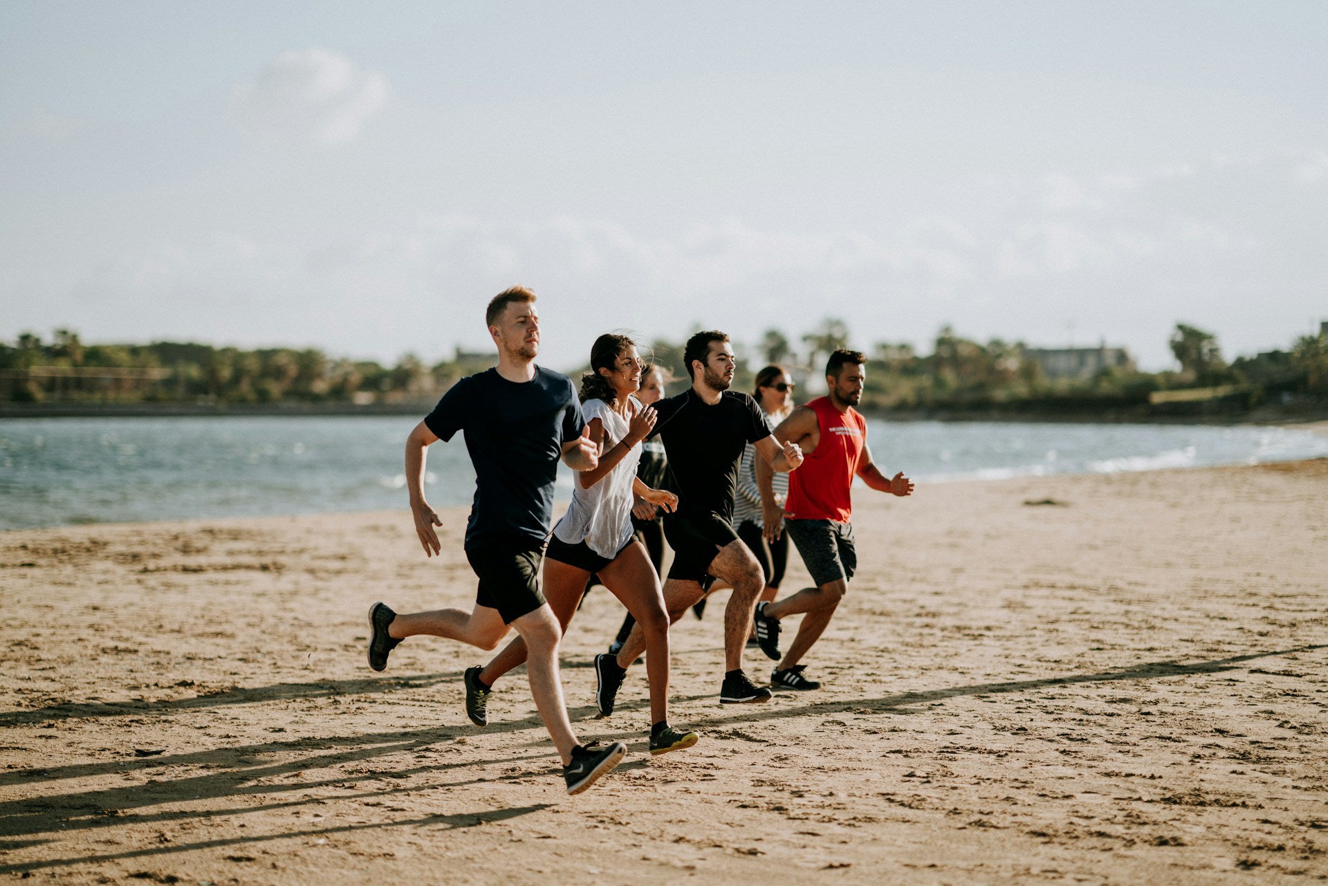 A small group of people jogging on the beach in the middle of the day.